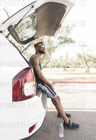 Black man sitting on car hatchback