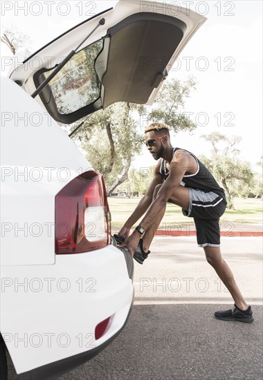 Black man leaning on car hatchback stretching leg