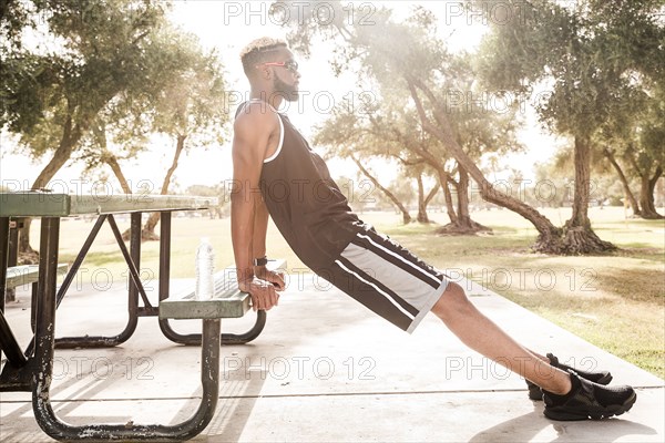 Black man leaning on picnic table in park stretching legs