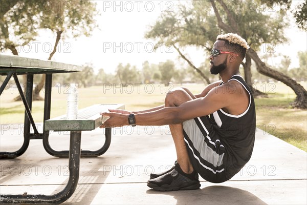 Black man holding picnic table in park stretching arms