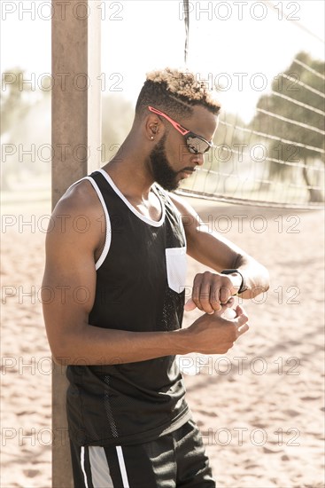 Black man leaning on beach volleyball net checking the time