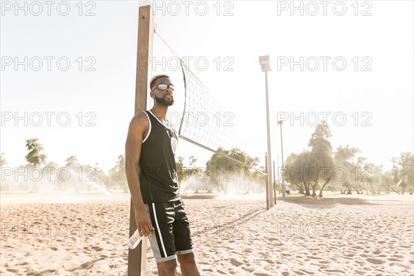 Black man leaning on beach volleyball net