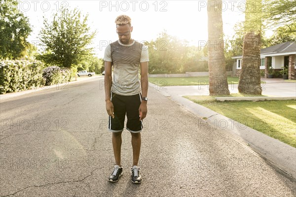 Black man standing on street in the neighborhood looking down