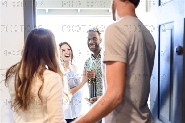 Couple greeting friends bringing wine bottle at door