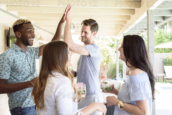 Smiling friends with cold drinks high-fiving outdoors