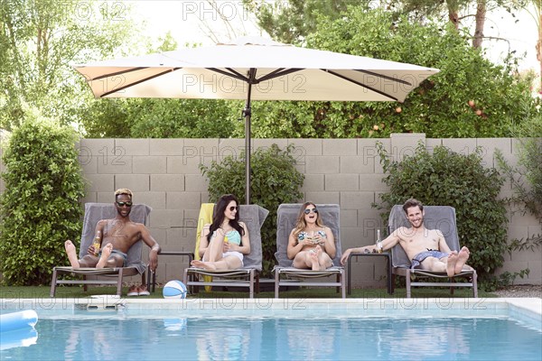 Smiling friends relaxing and drinking poolside