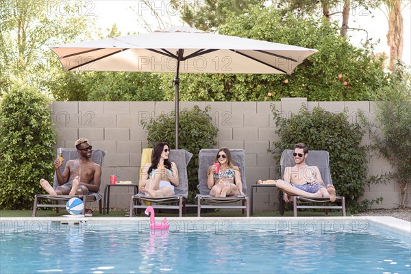 Smiling friends relaxing and drinking poolside