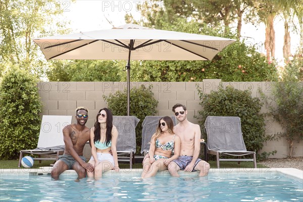 Smiling friends sitting and relaxing poolside