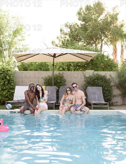 Smiling friends sitting and relaxing poolside