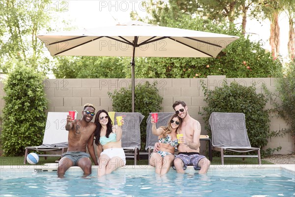 Smiling friends sitting and toasting poolside