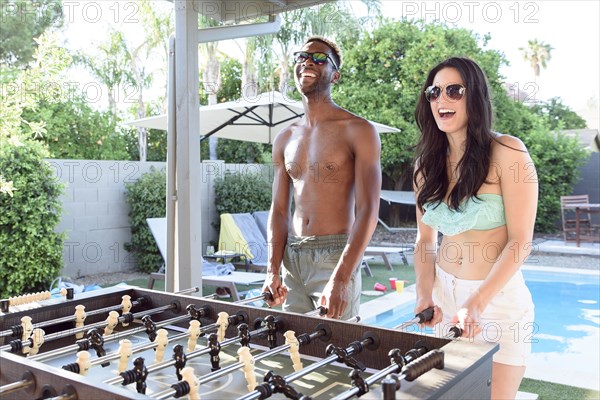 Couple playing foosball outdoors near swimming pool