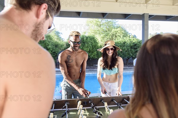 Friends playing foosball outdoors near swimming pool