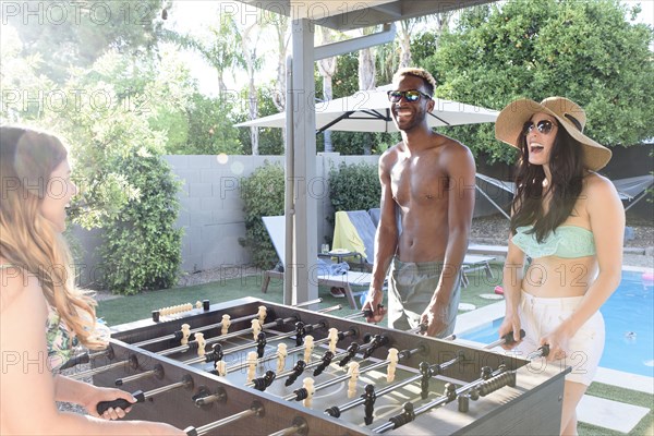 Friends playing foosball outdoors near swimming pool