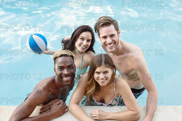 Portrait of smiling friends in swimming pool with basketball