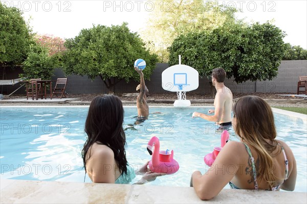 Women watching men playing basketball in swimming pool