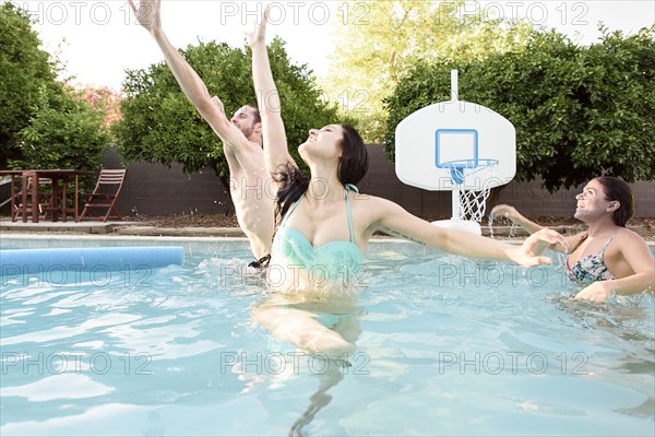 Caucasian friends playing basketball in swimming pool