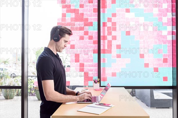 Caucasian man typing on laptop and listening to headphones