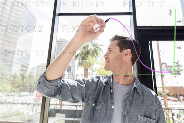 Caucasian man drawing diagram on glass wall