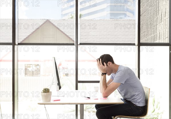 Frustrated Caucasian man with head in hands at desk