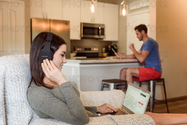 Caucasian woman sitting in armchair using laptop listening to headphones