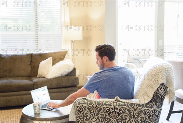 Caucasian man sitting in armchair using laptop and drinking coffee