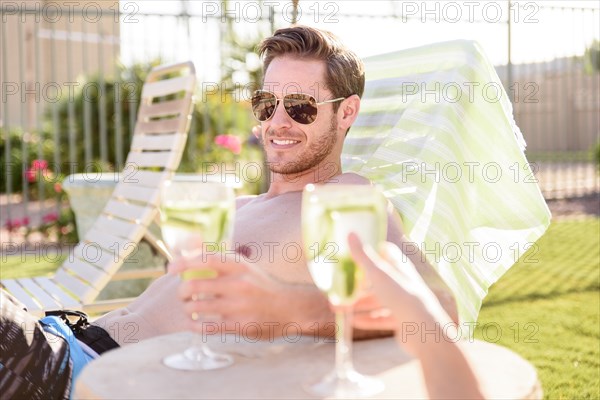 Caucasian couple relaxing in lounge chairs holding drinks