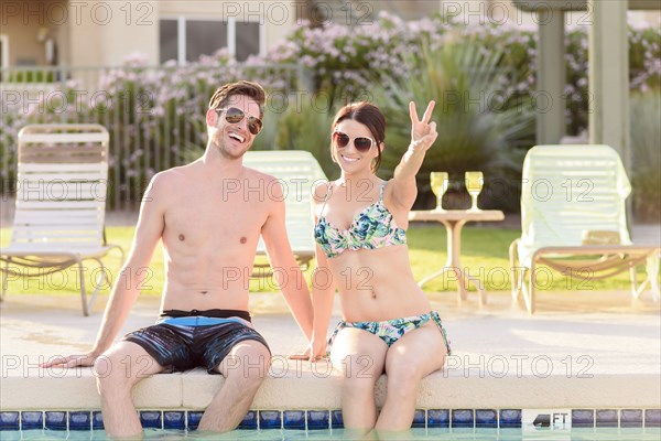 Portrait of Caucasian couple sitting at edge of swimming pool