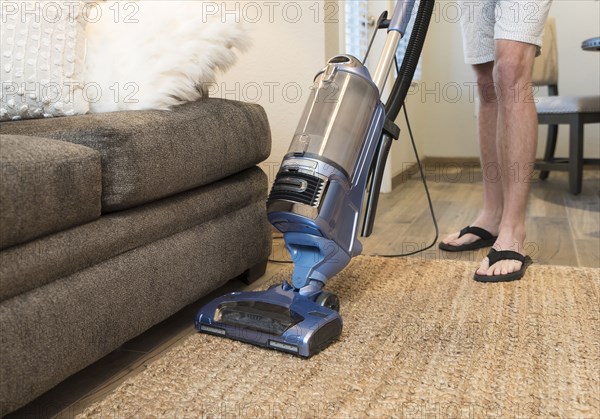 Legs of Caucasian man vacuuming rug near sofa