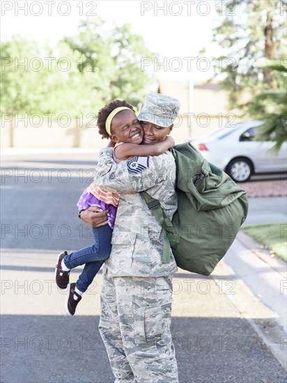 Black woman soldier hugging daughter in street