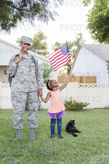 Smiling black woman soldier with daughter waving American flag