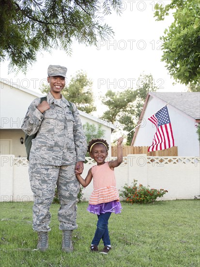 Smiling black woman soldier with daughter waving American flag