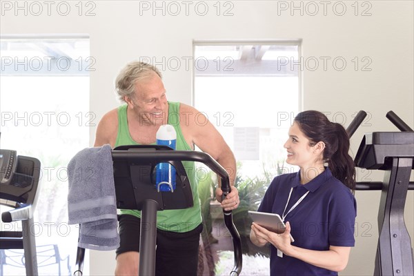 Caucasian trainer holding digital tablet watching man exercise