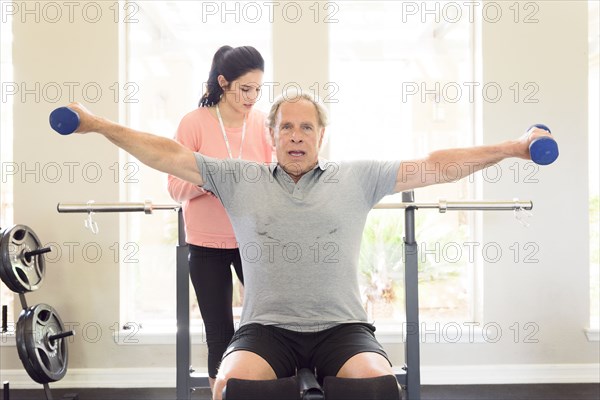 Caucasian trainer watching man lifting dumbbells