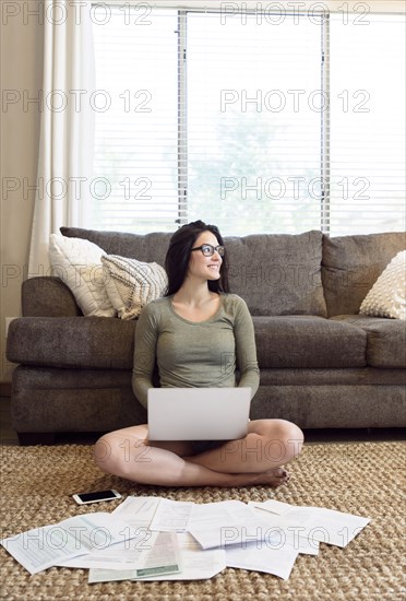 Caucasian woman sitting on floor using laptop near paperwork