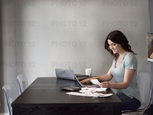 Caucasian woman holding receipt and using laptop