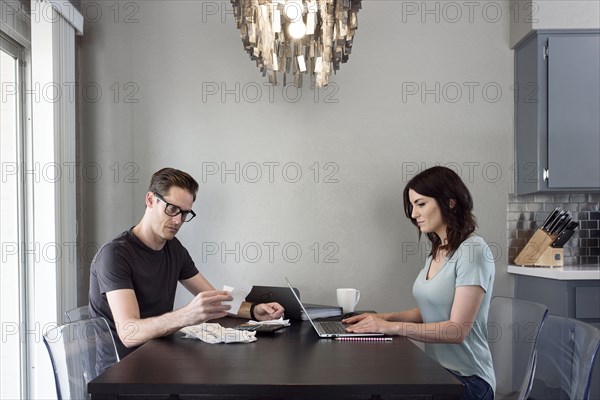 Caucasian man reading receipt while woman uses laptop