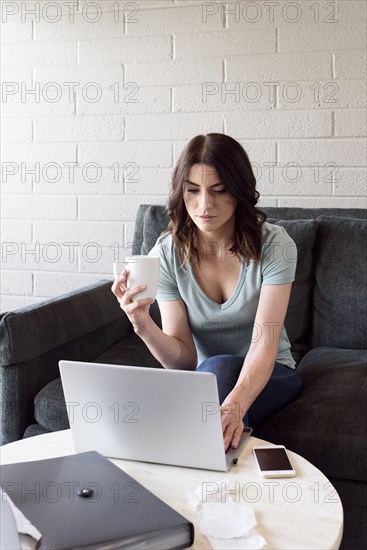 Caucasian woman drinking coffee and using laptop