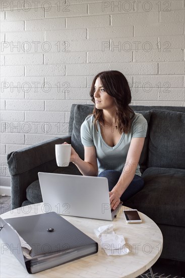 Caucasian woman drinking coffee and using laptop