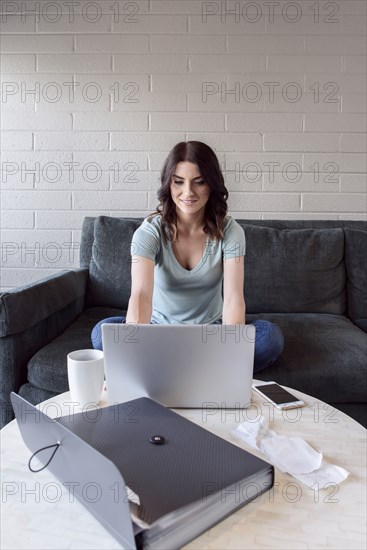 Caucasian woman sitting on sofa using laptop