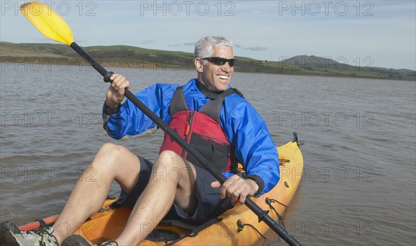 Middle-aged man rowing a kayak in still water
