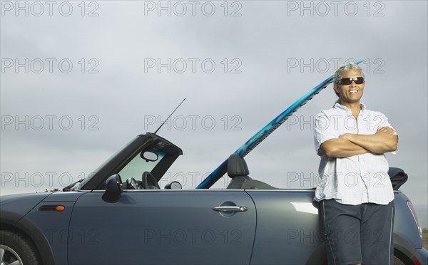 Senior man leaning on a convertible with a surfboard in it