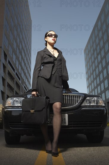 Asian businesswoman with briefcase standing at front of car