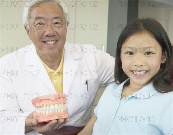 Senior Asian male dentist showing model of teeth to young patient