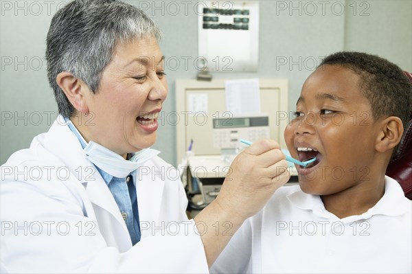 Senior Asian female dentist examining young male patient