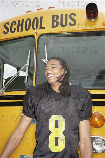 Young African man in football uniform next to school bus