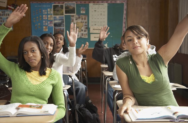 Group of students with hands raised in classroom