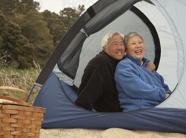 Senior Asian couple sitting in tent smiling