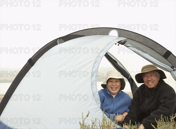 Senior Asian couple sitting in tent smiling