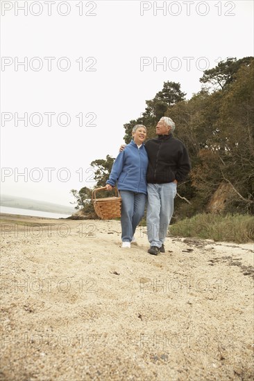 Senior Asian couple walking on beach with picnic basket