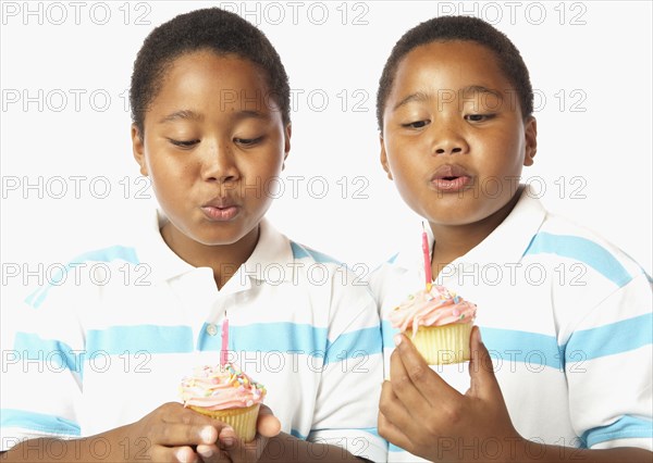 Young African twin brothers holding cupcakes with candles